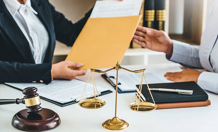 Lawyer handing a folder to a client beside a gavel and scales of justice