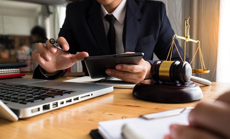 Lawyer using a tablet beside a laptop, gavel, and scales of justice